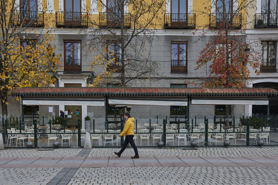 Una persona pasea al lado de una mampara instalada en un restaurante de la Plaza de Oriente, en Madrid (España).