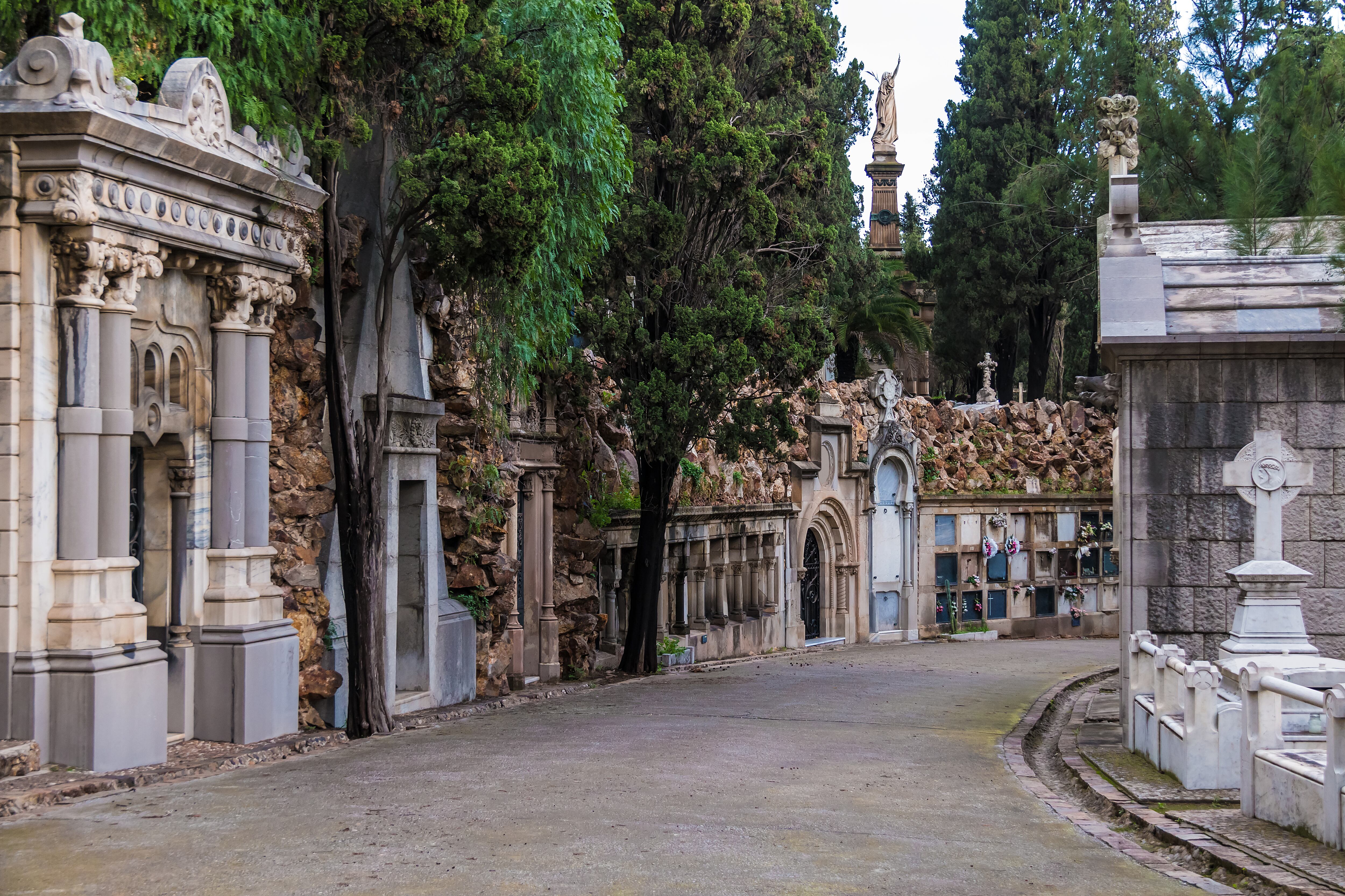 Perspective view of the curved footpath with graves and crypts on the Montjuic Cemetery in overcast day, Barcelona, Catalonia, Spain