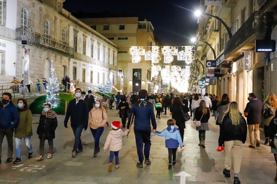 Transeúntes pasean bajo las luces navideñas con mascarilla en Vigo