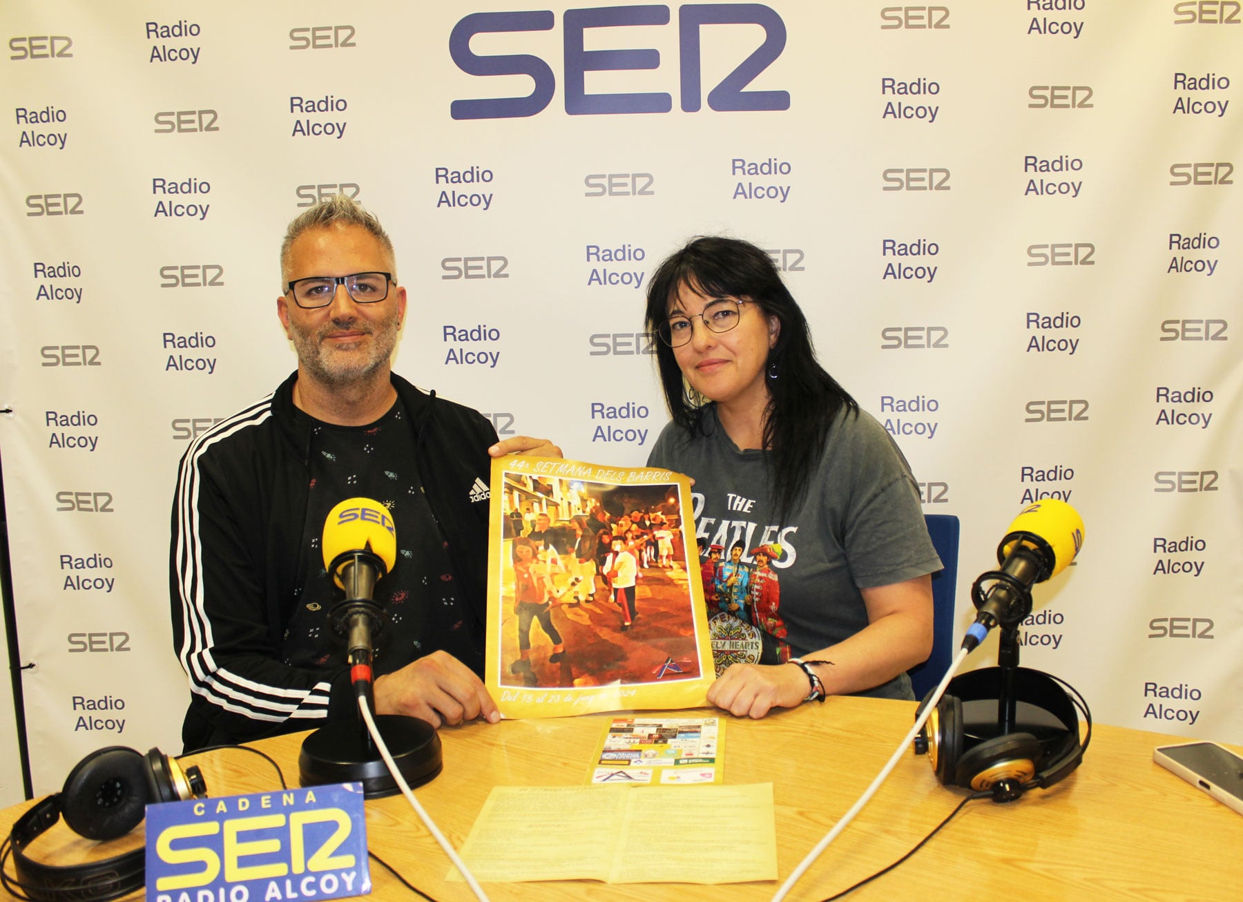 Toni Dávila i Aurora Cedrón, en l'estudi central de Radio Alcoy sujectant un cartell de les festes