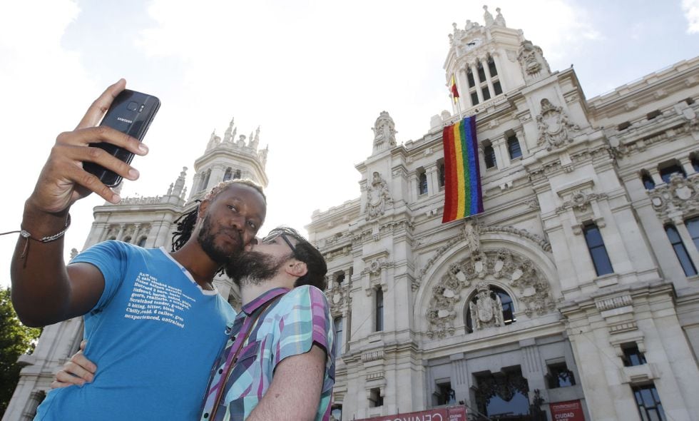 Una pareja se fotografía junto a la fachada del Ayuntamiento de Madrid donde hoy se ha desplegado la bandera del orgullo gay.