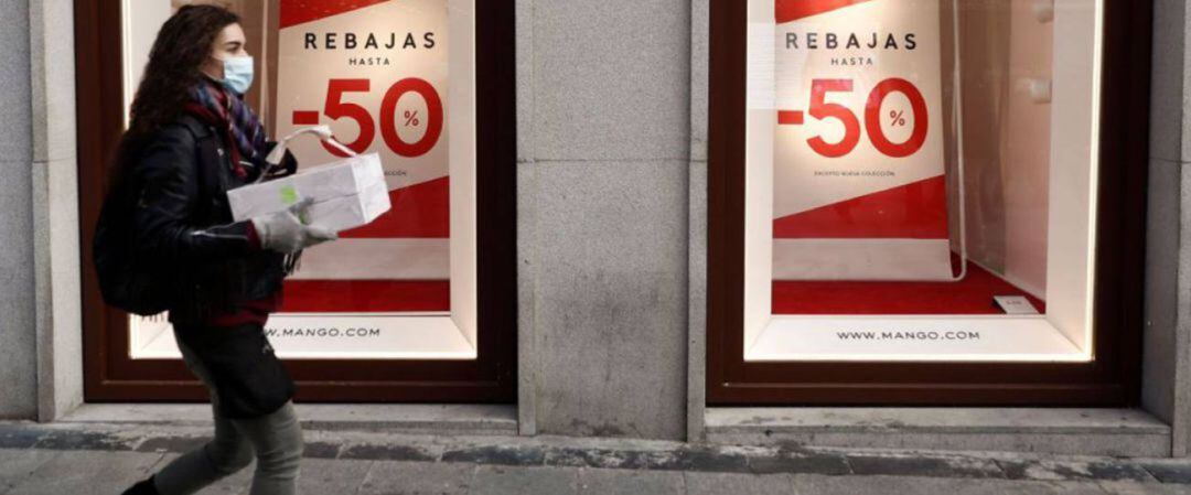 Una mujer pasea con un paquete delante de un escaparate en Rebajas.