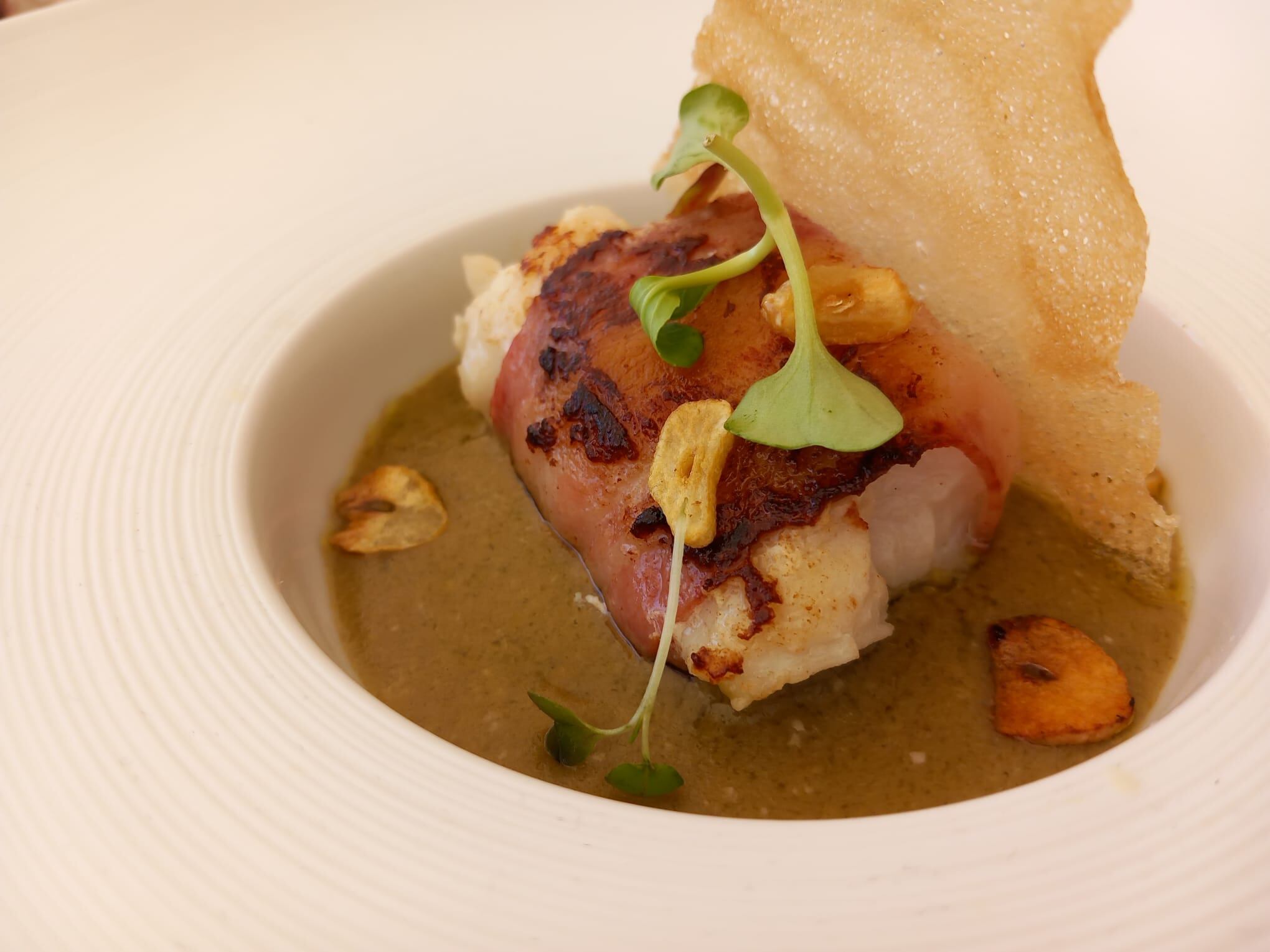 Merluza albardada con velo ibérico y emulsión de guisote gastoreño