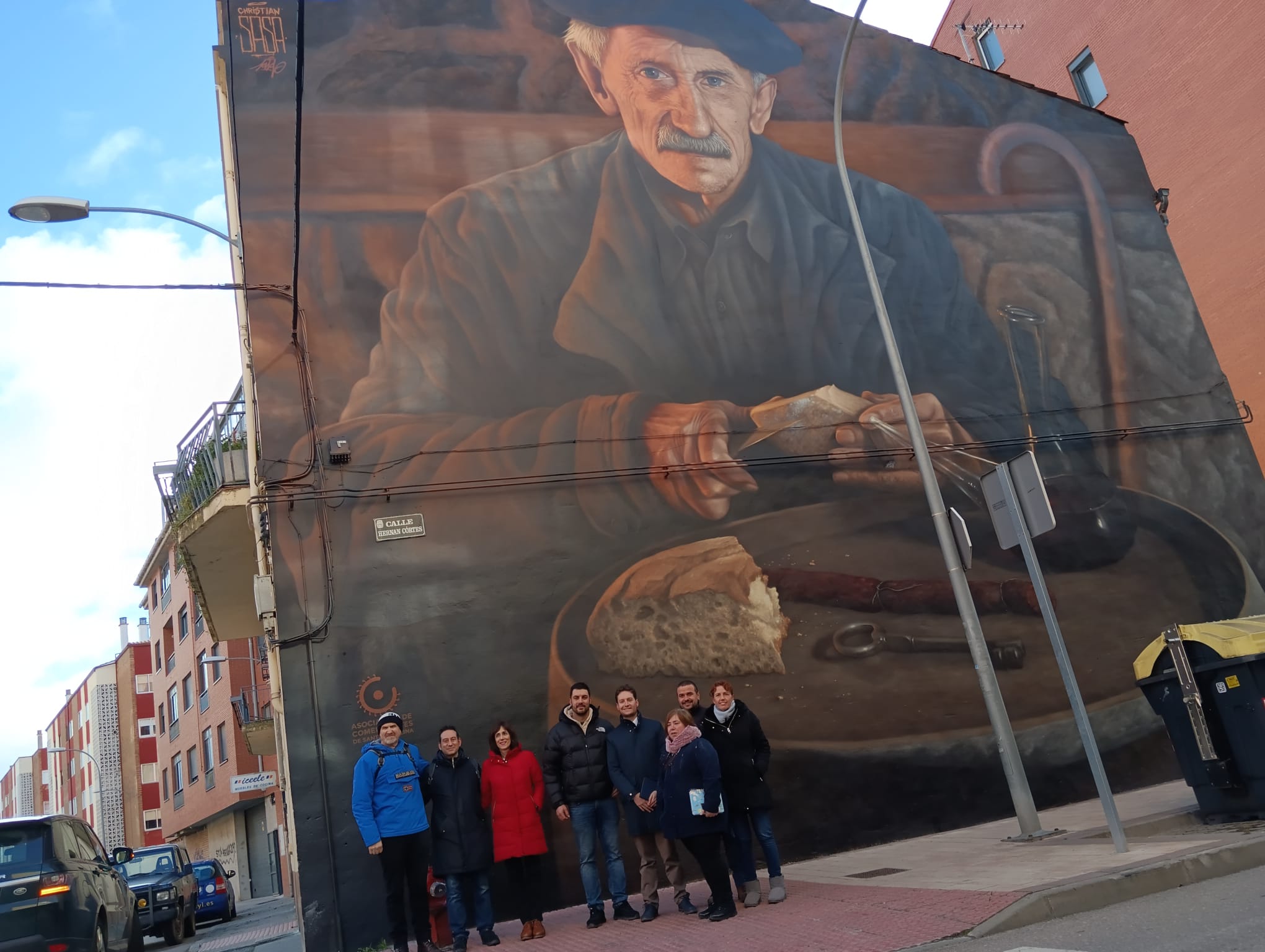 Representantes del Ayuntamiento y de la Asociación de Comerciantes de Santa Catalina posan, junto al autor, bajo el nuevo mural, situado en la calle Hernán Cortés