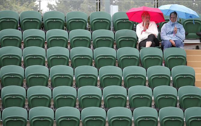 Dos espectadoras se protegen con paraguas después de que la lluvia retrasara el comienzo de uno de los partidos del torneo de tenis de Wimbledon en su tercera jornada