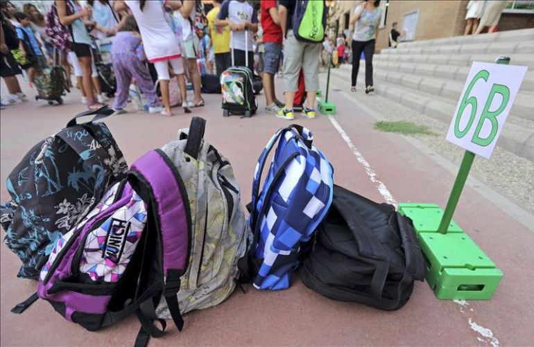 Varias mochilas apiladas en el patio de un colegio. 