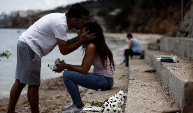 Un hombre besa a su hermana mientras un ramo de flores yace en el lugar donde un bebé de seis meses perdió la vida tras el incendio forestal de Mati, al noreste de Atenas (Grecia).