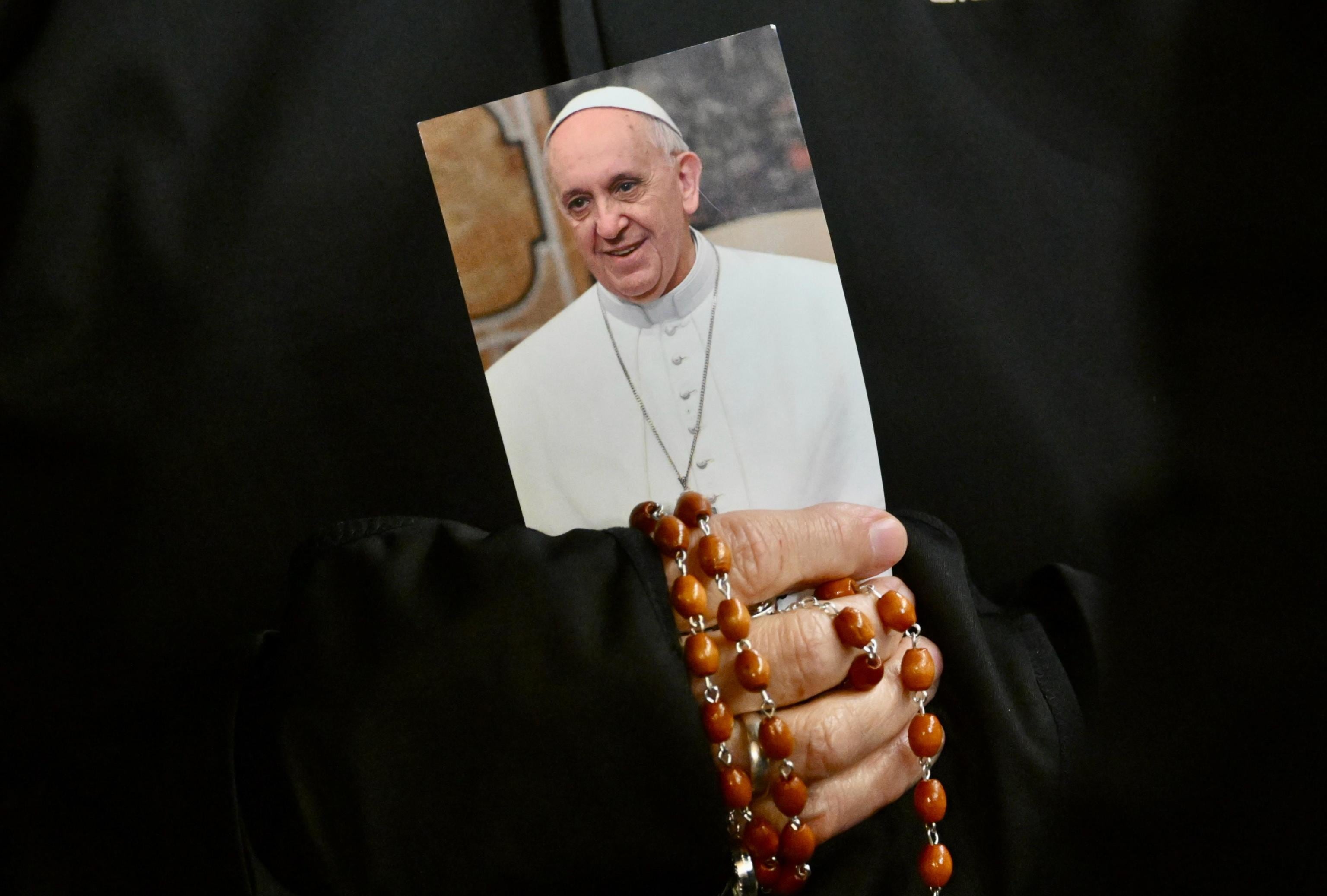 Una monja sostiene una imagen del papa Francisco y un rosario mientras los fieles asisten a una oración del Rosario por la salud del pontífice en la Plaza de San Pedro este lunes, en la Ciudad del Vaticano (Vaticano).