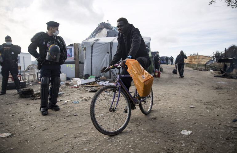 Agentes de policía galos observan a varios migrantes que son evacuados del campamento de Calais.