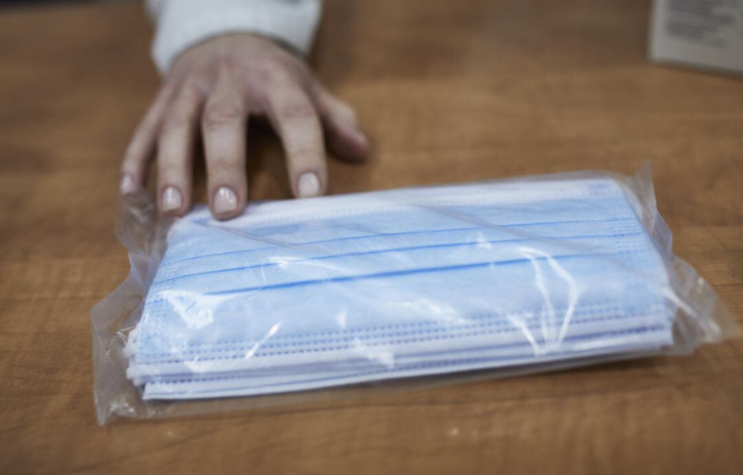 Una farmacéutica enseña a un cliente un paquete de mascarillas.