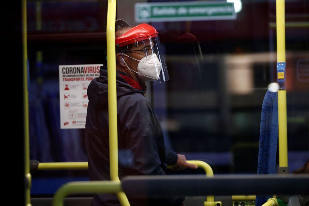 Un hombre protegido con mascarilla y una pantalla viaja en un autobús