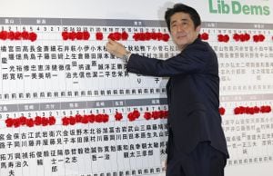 El primer ministro japonés Shinzo Abe, líder del partido demócrata liberal, sonrie mientras posicona una roseta en el nombre del candidato vencedor de su partido durante el recuento en la Camara nipona.