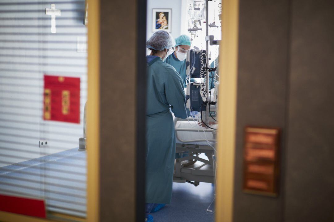 Dos trabajadores sanitarios totalmente protegidos atienden a un paciente en una camilla de la UCI de la Clínica Universidad de Navarra, en Pamplona