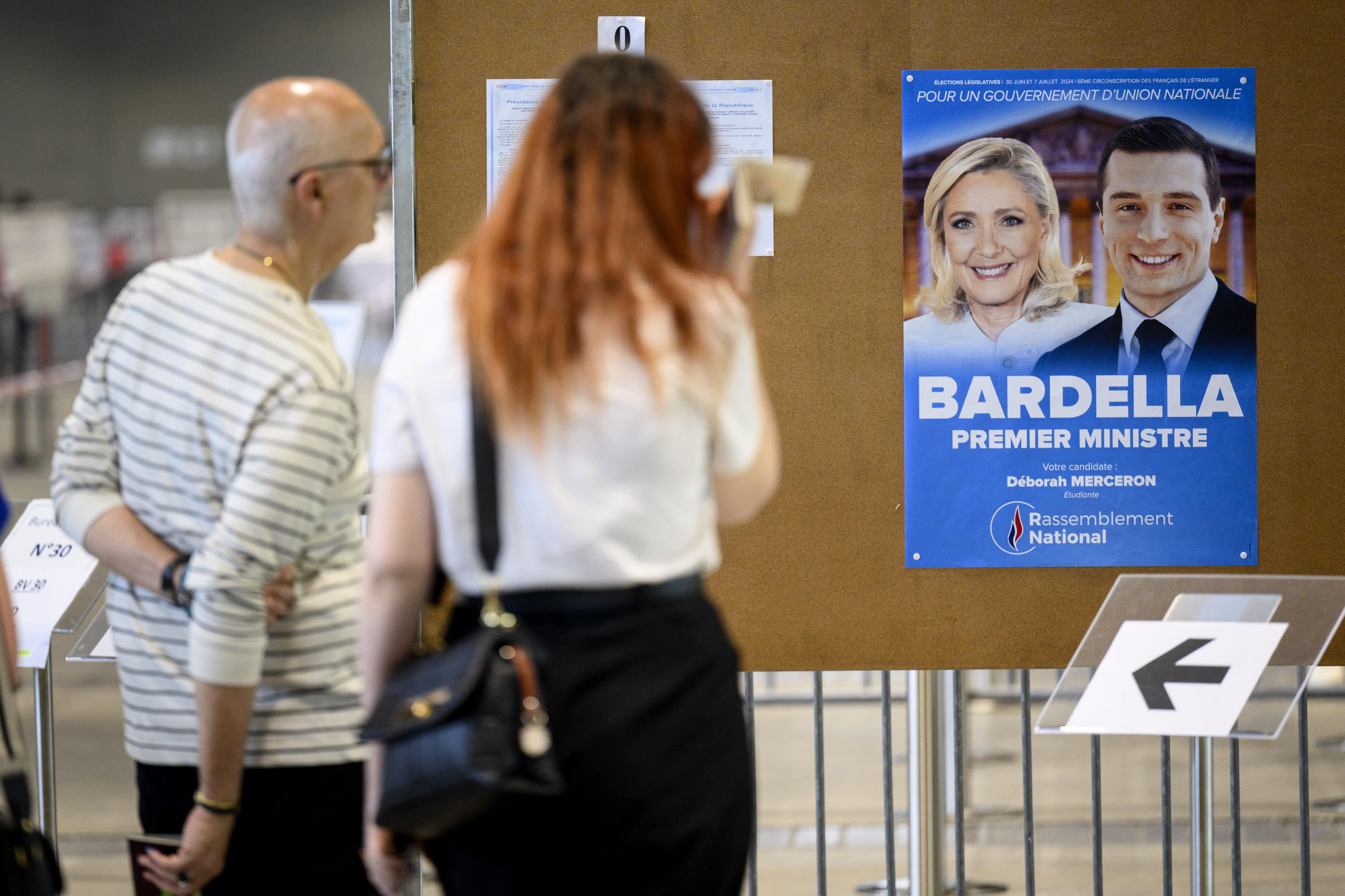 Dos electores frente al cartel de Bardella y Le Pen en un colegio electoral