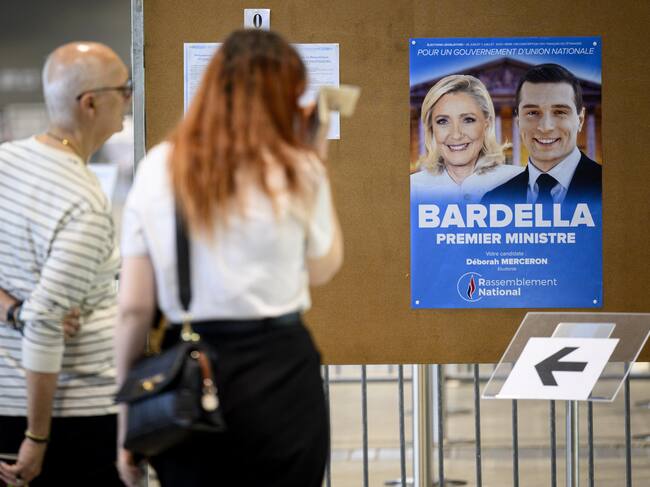 Dos electores frente al cartel de Bardella y Le Pen en un colegio electoral