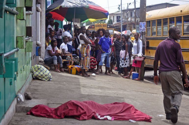 In this photo taken on Saturday, Nov. 22, 2014, the covered body, foreground, of a man suspected of dying from the Ebola virus, lies in the street as a person, right, walks past in the city center of Monrovia, Liberia.  As infection rates fall in Liberia,