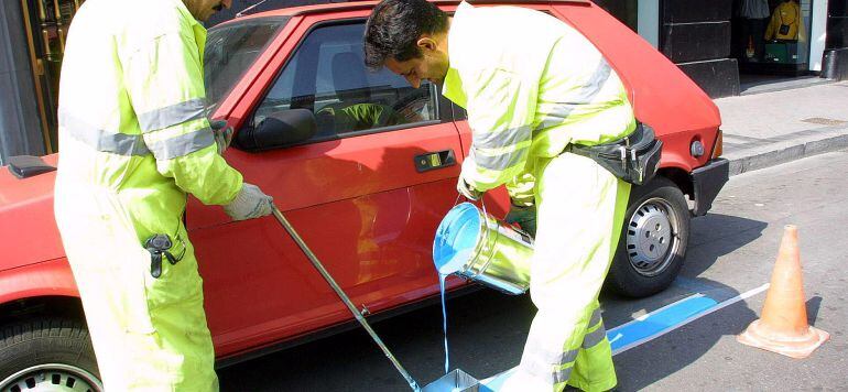 Dos trabajadores pintan la línea azul que delimita la ORA en una calle de Valladolid