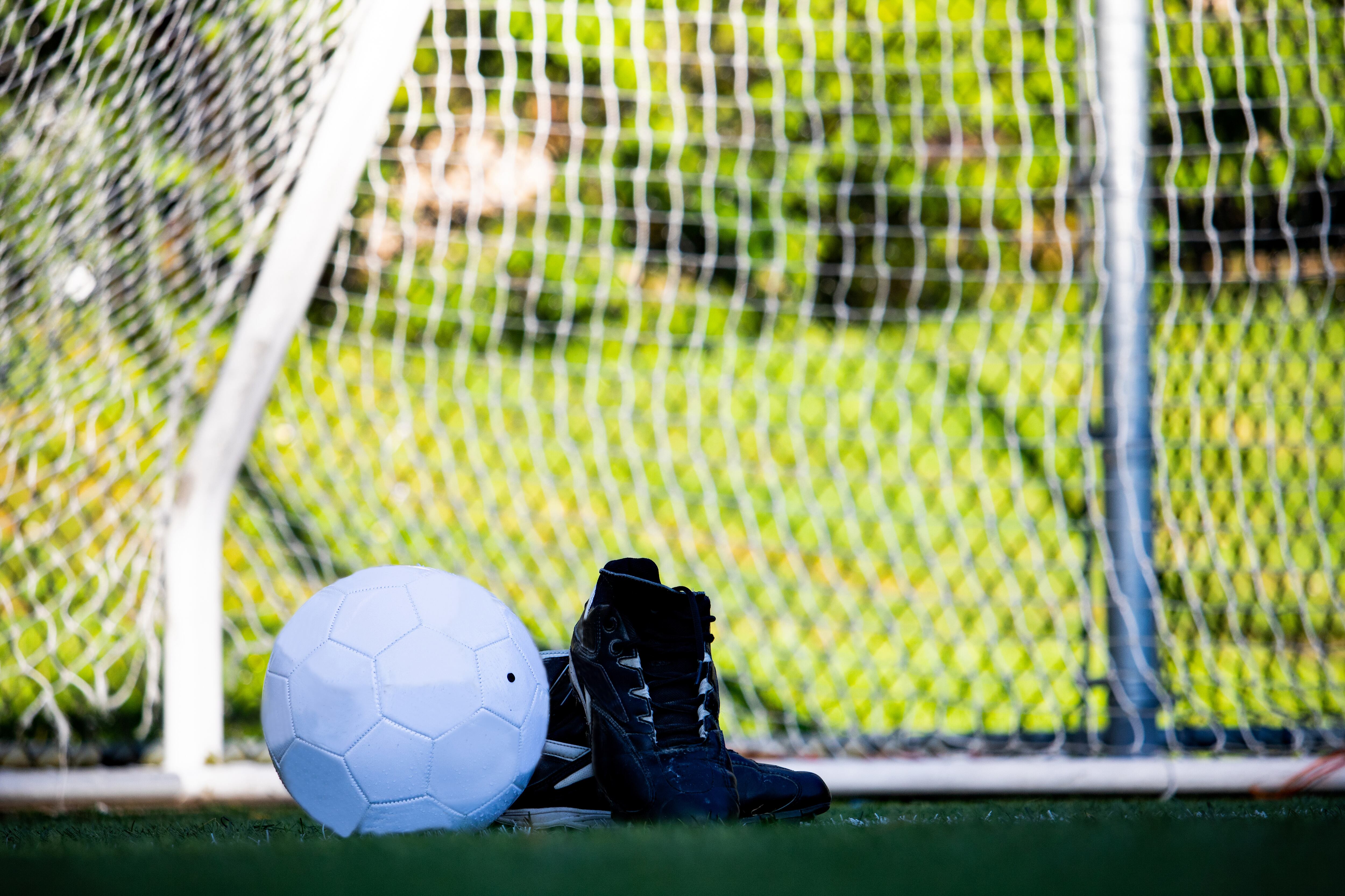 Balón blanco y botas negras en un campo de fútbol base.