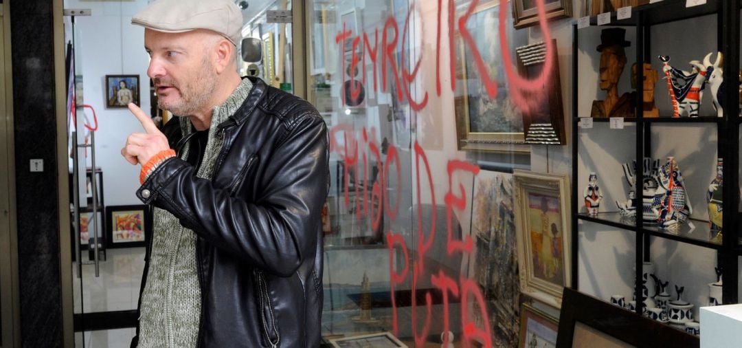 El artista Enrique Tenreiro, que el pasado miércoles dibujó una paloma de la paz y volcó un bote de pintura roja sobre la tumba de Franco, posa ante la pintada que ha aparecido hoy en la cristalera de la galería ArtBy&#039;s de A Coruña