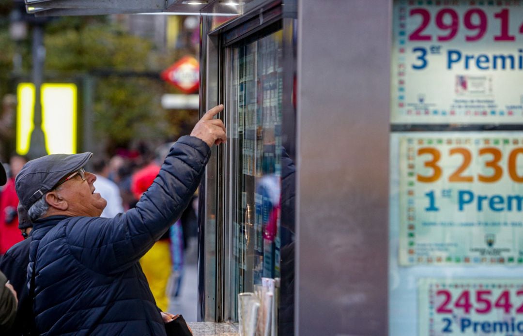 Un hombre consulta varios décimos en una administración de lotería.