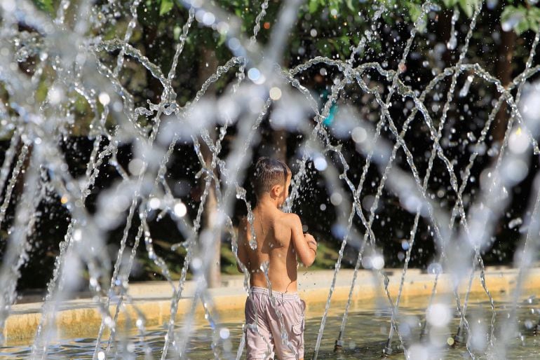 Un niño juega con los chorros de agua para refrescarse en un parque.