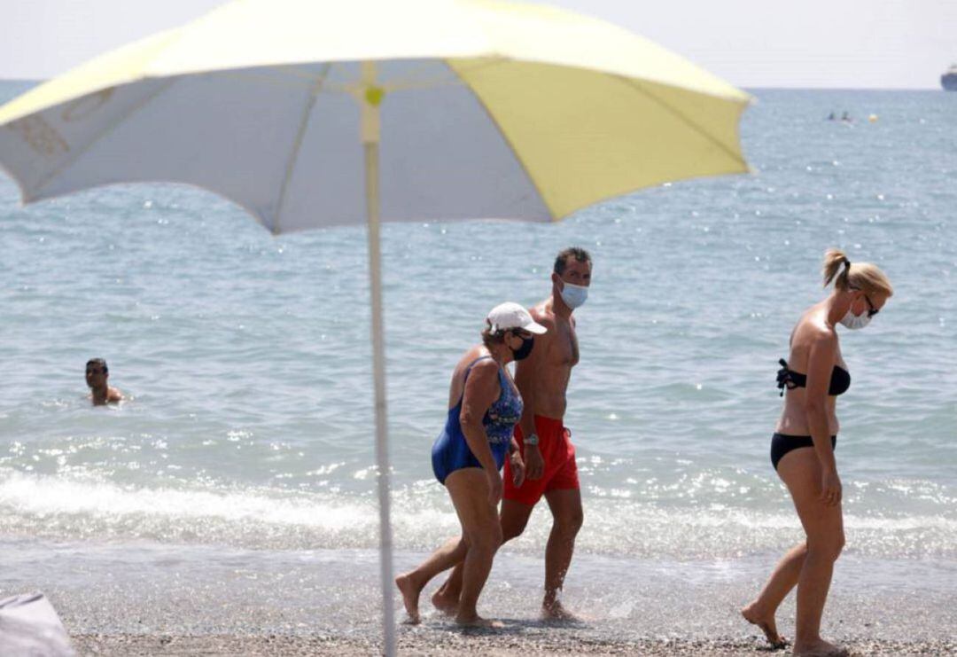 Archivo - Bañistas con mascarilla pasean por la orilla de una playa