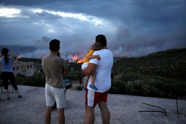 Un hombre abraza a su hijo mientras ve Rafina en llamas.