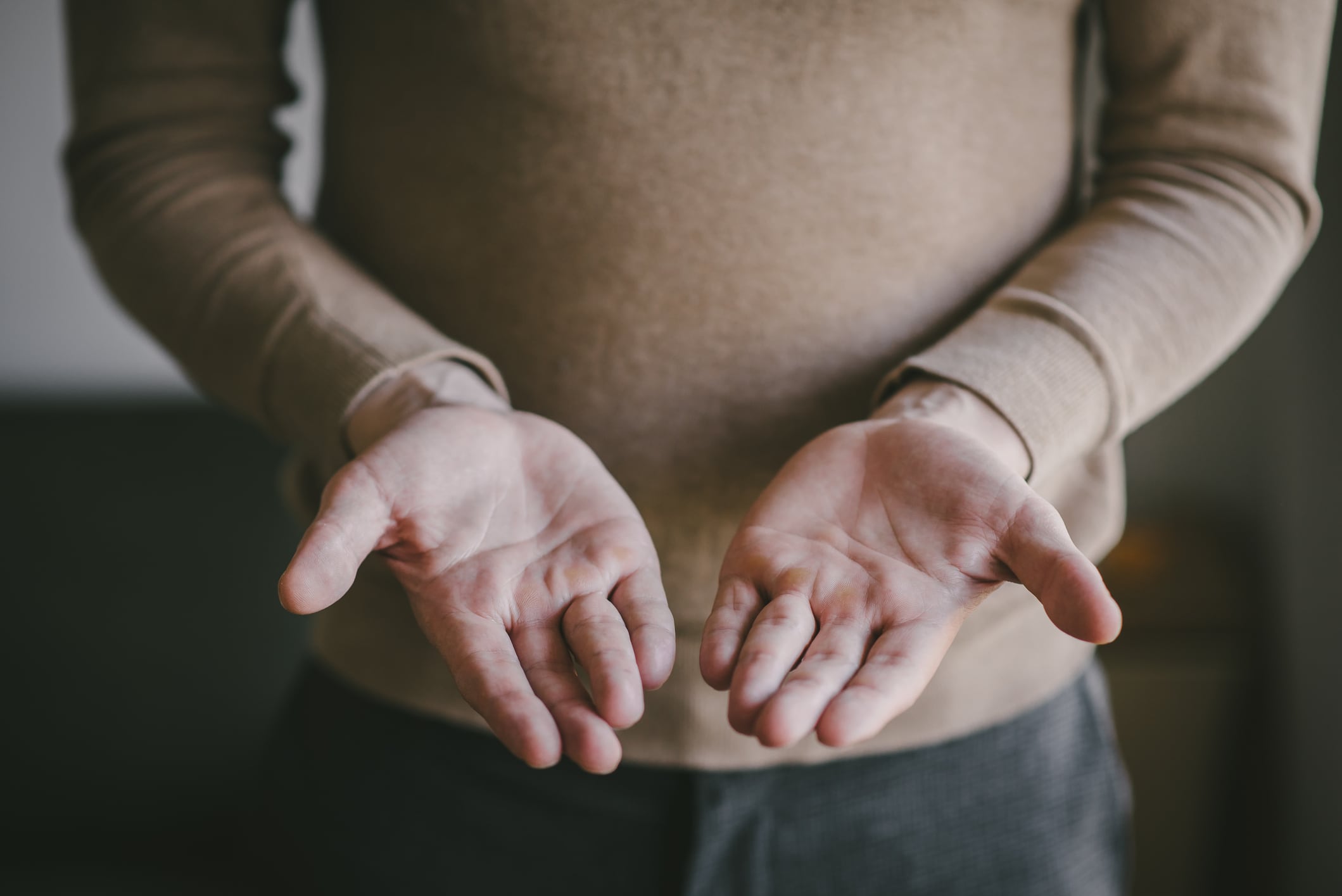 Man in brown sweater offers two clean hands and holds nothing close-up background