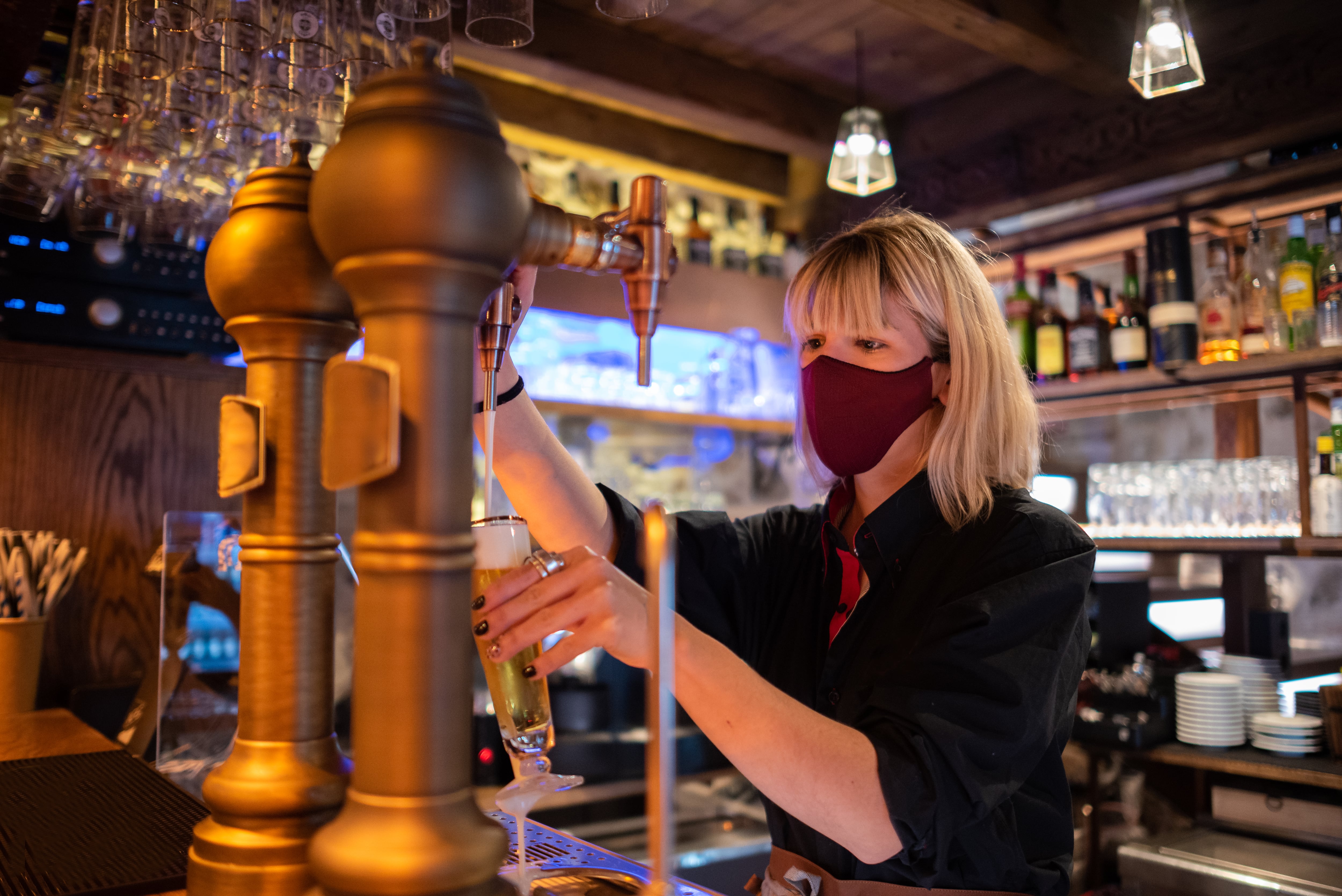 Waitress wearing a mask serving a beer from tap in the new normal