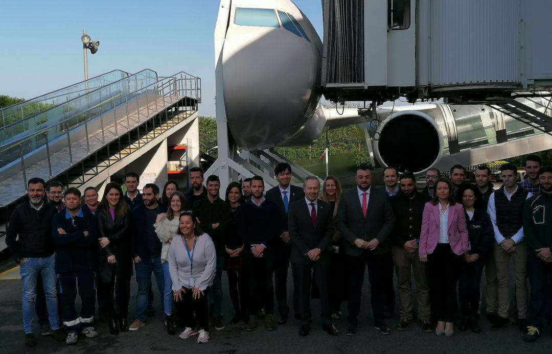 El presidente del Principado, Adrián Barbón, junto al director del centro de I+D y trabajadores posan delante de una pasarela de embarque. 