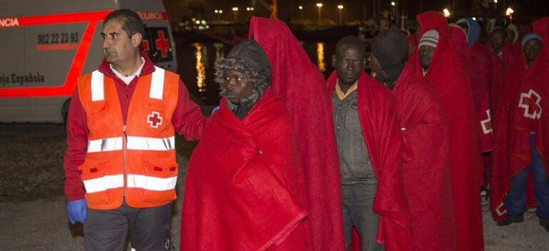 Un miembro de la Cruz Roja acompaña a los subsaharianos que han desembarcado en el puerto de Motril después de que Salvamento Marítimo les rescatara a unas 56 millas de la costa de Granada cuando navegaban en una patera.