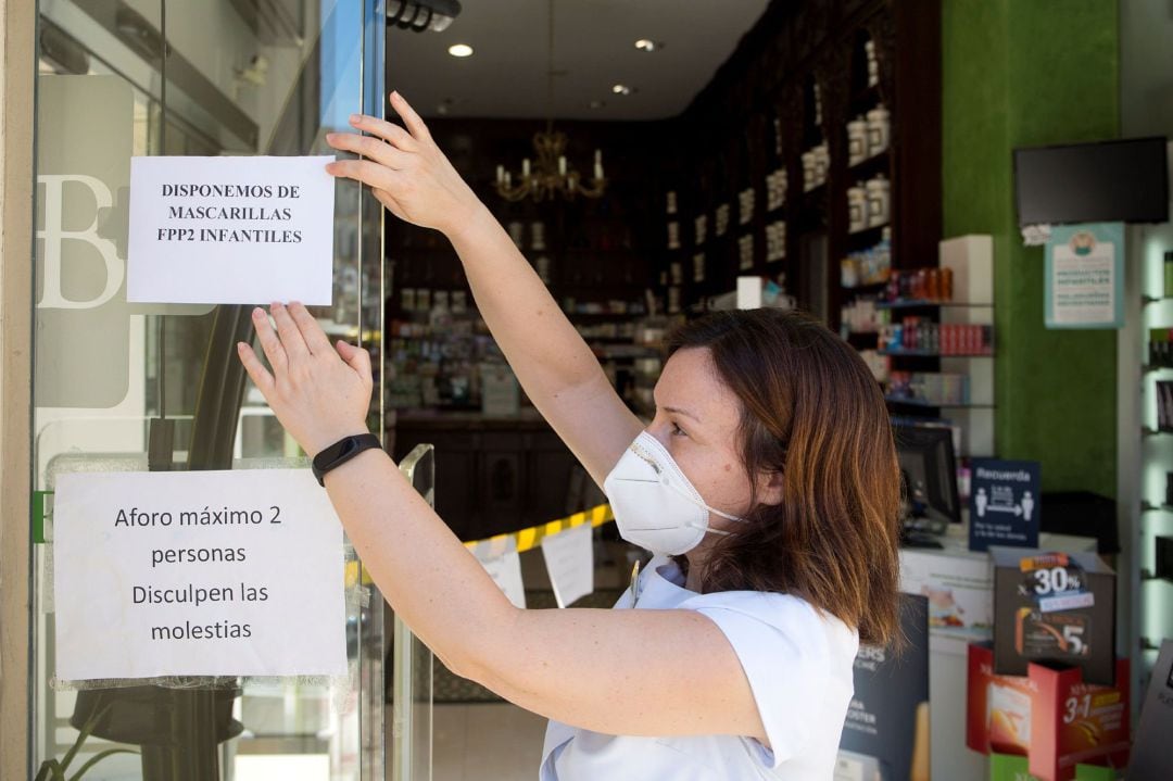 Empleada de farmacia poniendo el cartel de disponible mascarilla