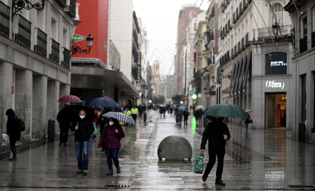 Varias personas caminan protegidas por una vía de la capital el mismo día de la llegada del temporal ‘Gaetán’, en Madrid.