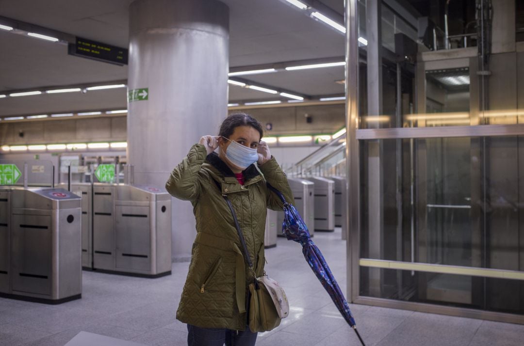 Una mujer se pone una mascarilla tras recibirla de Protección Civil a la entrada del metro