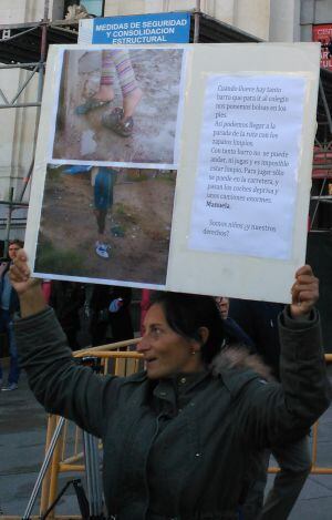 Una de las mujeres que vive en El Gallinero con uno de los carteles utilizados en la protesta frente al Ayuntamiento. Cuando hay barro los niños tienen que ir al colegio con bolsas de plástico.