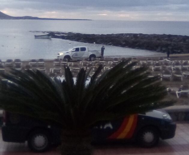 Al fondo, la patera que ha llegado esta mañana a la playa de Las Vistas, en Los Cristianos (Tenerife), cerca de las ocho de la mañana