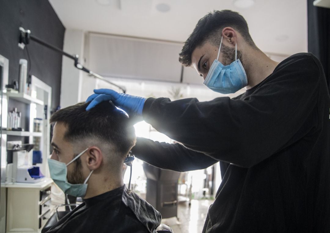 Un peluquero atiende a un cliente en su peluquería