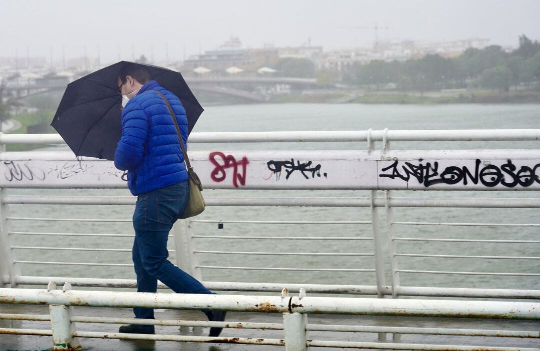 Un persona se protege de la lluvia y el viento caminando por una pasarela  peatonal.