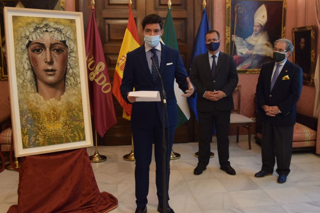 El joven pintor Manuel Peña Suárez explica su obra ante la mirada de Juan Carlos Cabrera, delegado municipal de Fiestas Mayores, y José Antonio Fernández Cabrero, hermano mayor de La Macarena