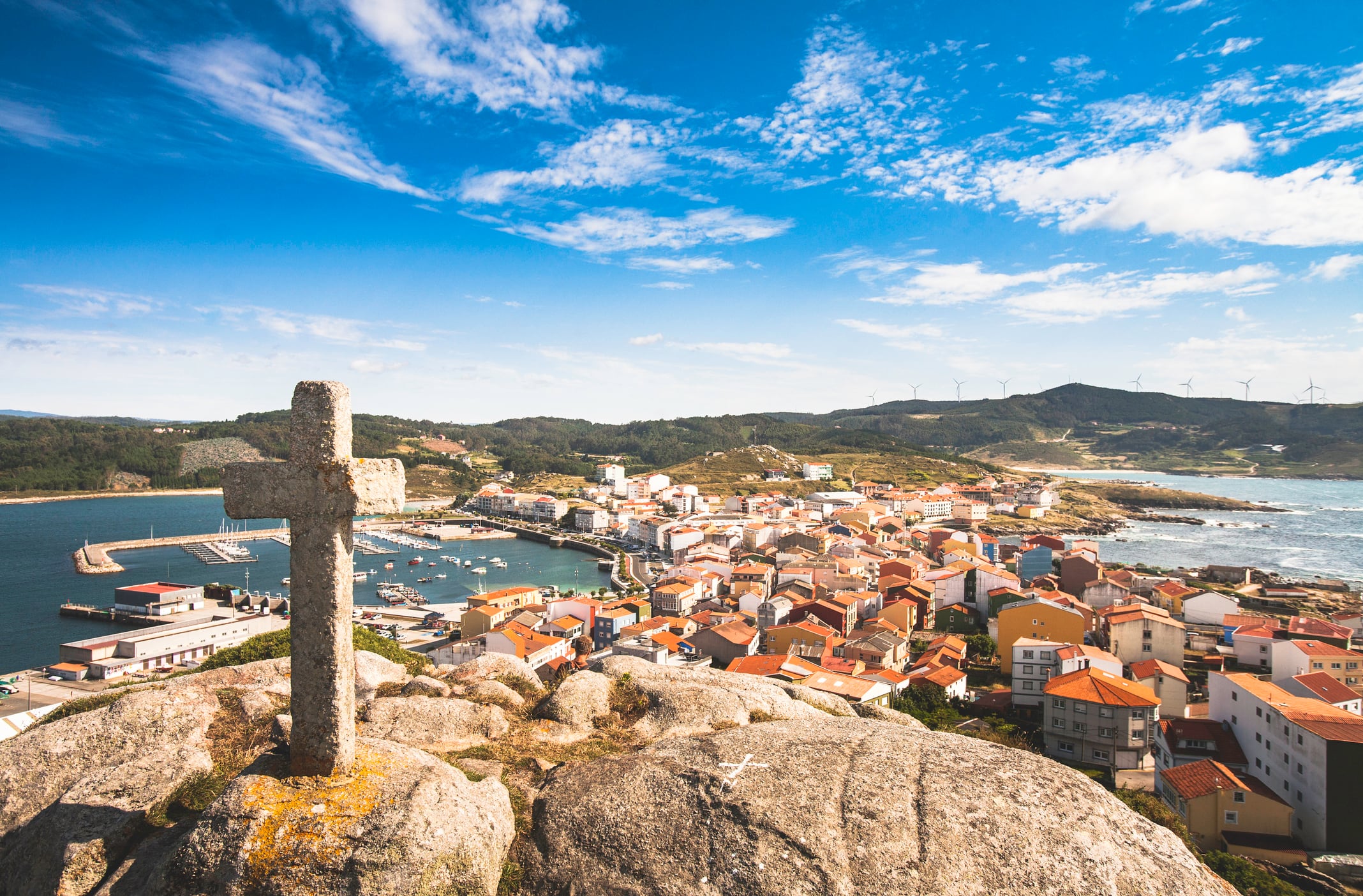 The fishing village of Muxía on the Costa da Morte of Galicia, Spain. A stone crucifix at the top of the peninsula overlooks the town and its narrow rocky branch out into the Atlantic ocean. Muxía is a popular finishing spot along the Camino de Santiago for pilgrims who wish to complete their walk at the coast.