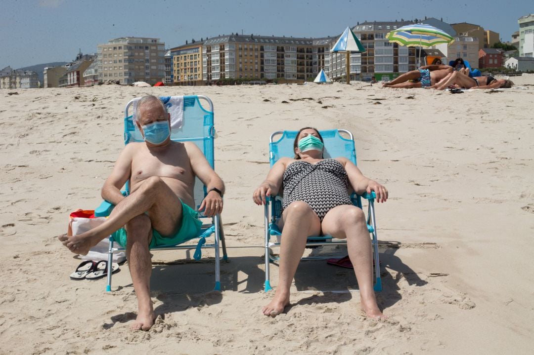 Dos personas protegidas con mascarillas toman el sol en la Playa de A Rapadoira en Foz, en la comarca de A Mariña, Lugo.