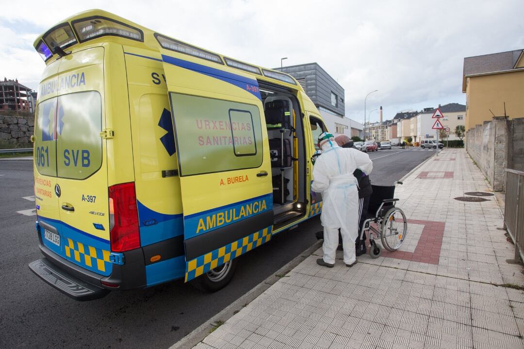 Un trabajador sanitario totalmente protegido ayuda a subir a la ambulancia a un anciano.