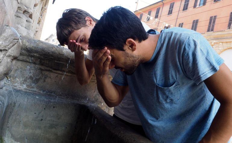 Dos chicos mojan su cara en una fuente para combatir las altas temperaturas 