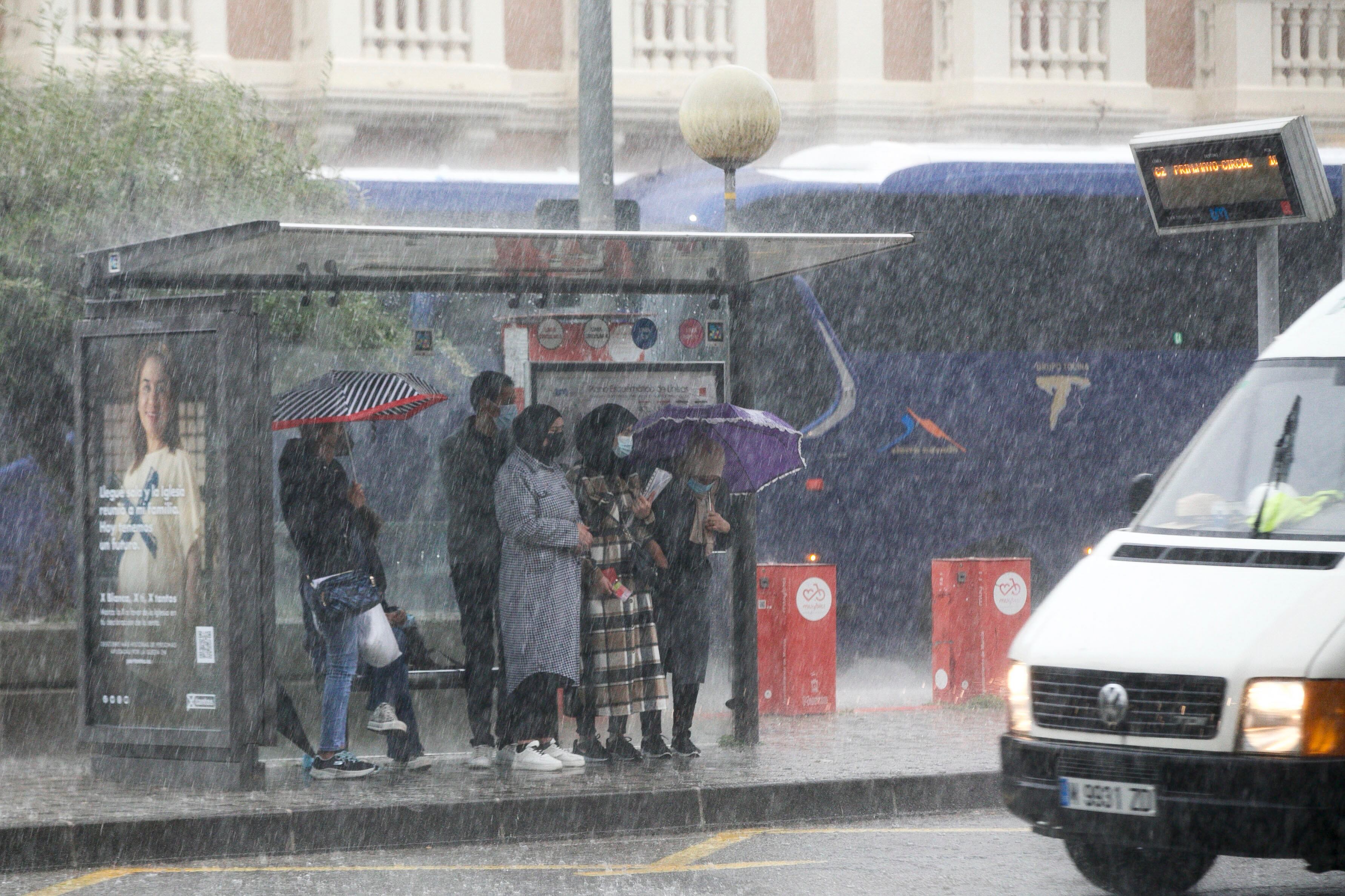 Varios ciudadanos se protegen en una parada de autobús de las lluvias torrenciales que caen este miércoles sobre Murcia capital. EFE/Juan Carlos Caval