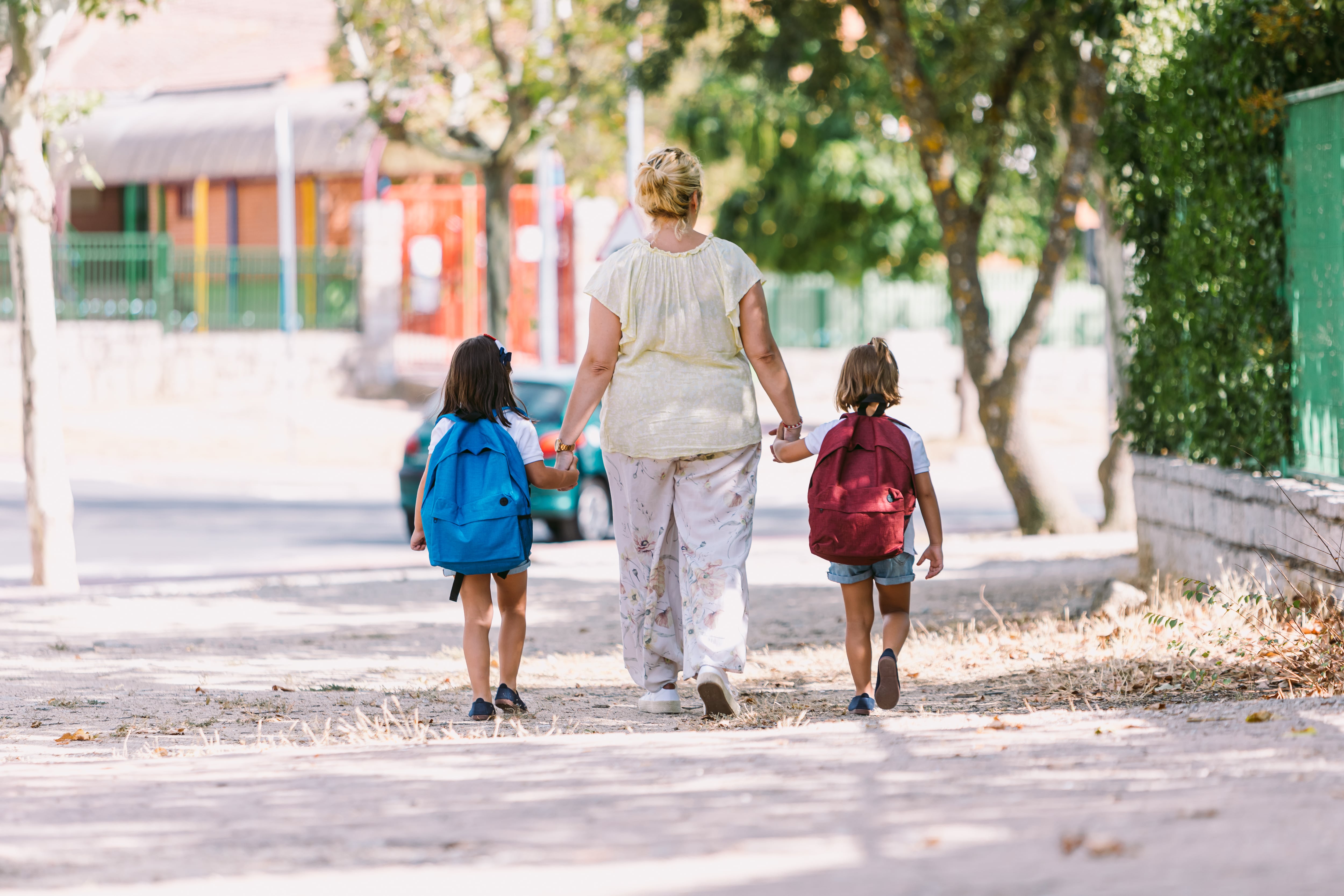 Mother and daughters with their backs turned, go hand in hand on the way to school. Concept of education and back to school.