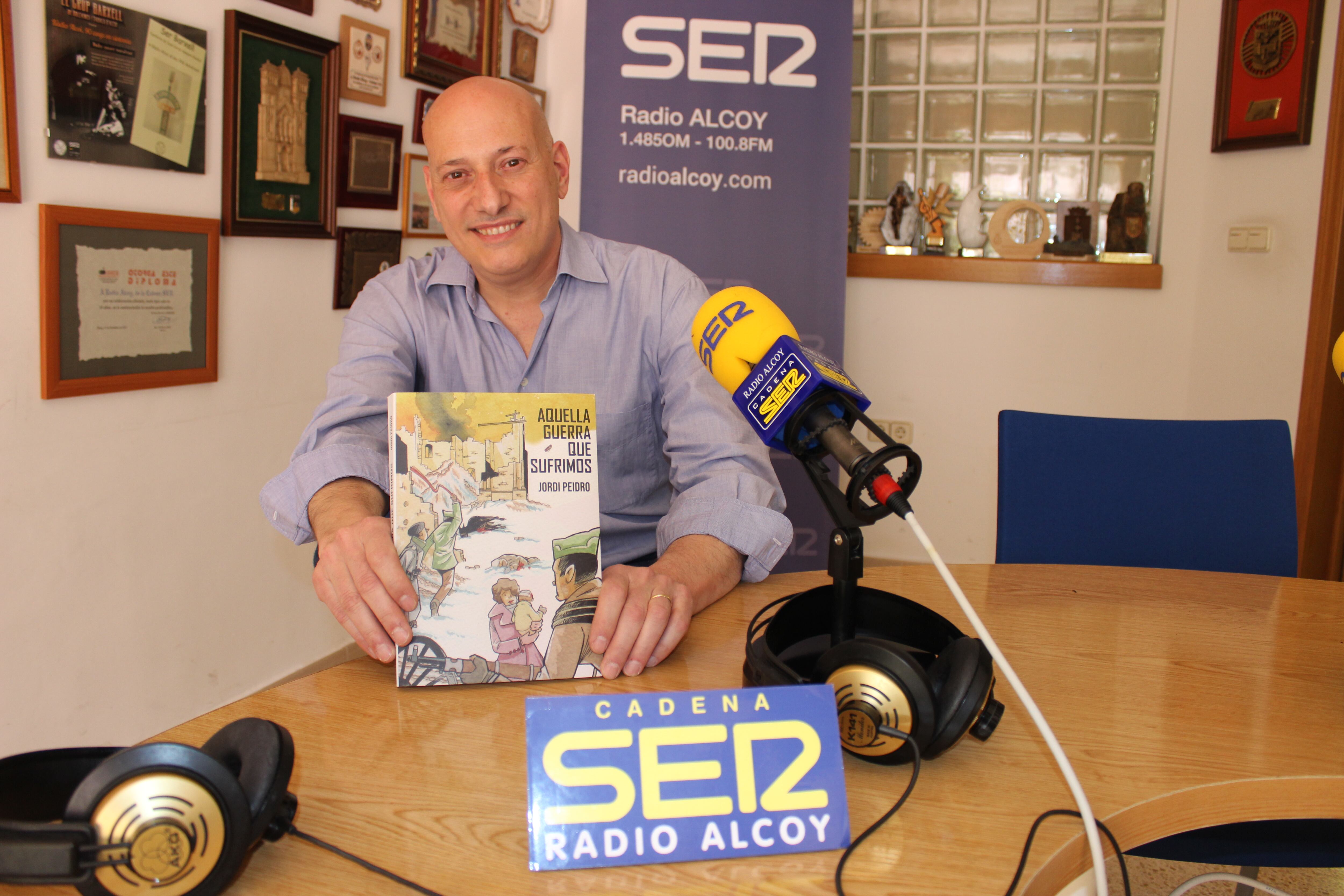 Jordi Peidro, en el estudio central de Radio Alcoy, muestra un ejemplar de su novela gráfica 'Aquella guerra que sufrimos'