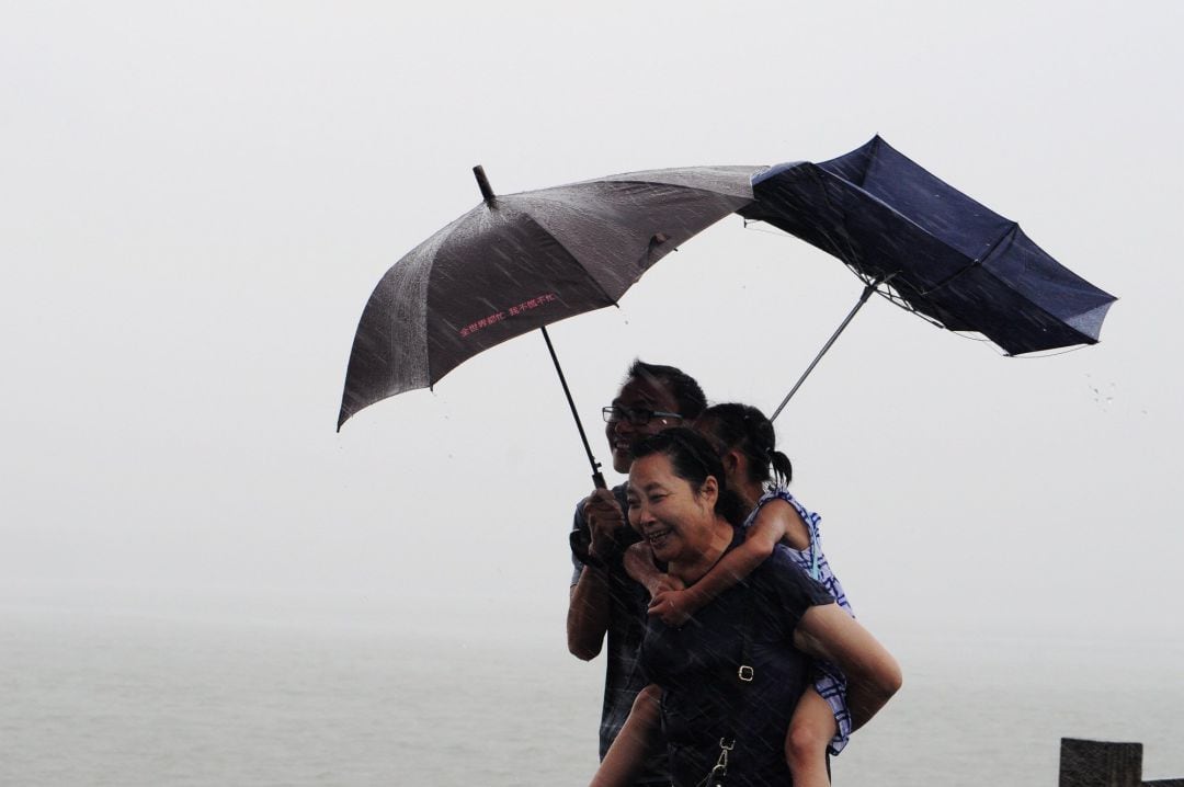 Dos adultos y una niña se protegen con sus paraguas a unas horas de la llegada del tifón en Hangzhou, China.