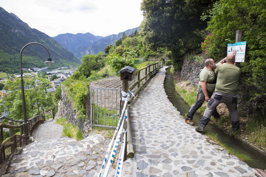 Dos operaris del comú d'Andorra la Vella pengen els cartells que senyalitzen el sentit únic del camí del Rec del Solà que demà es reobre al públic coincidint amb l'ampliació del desconfinament.