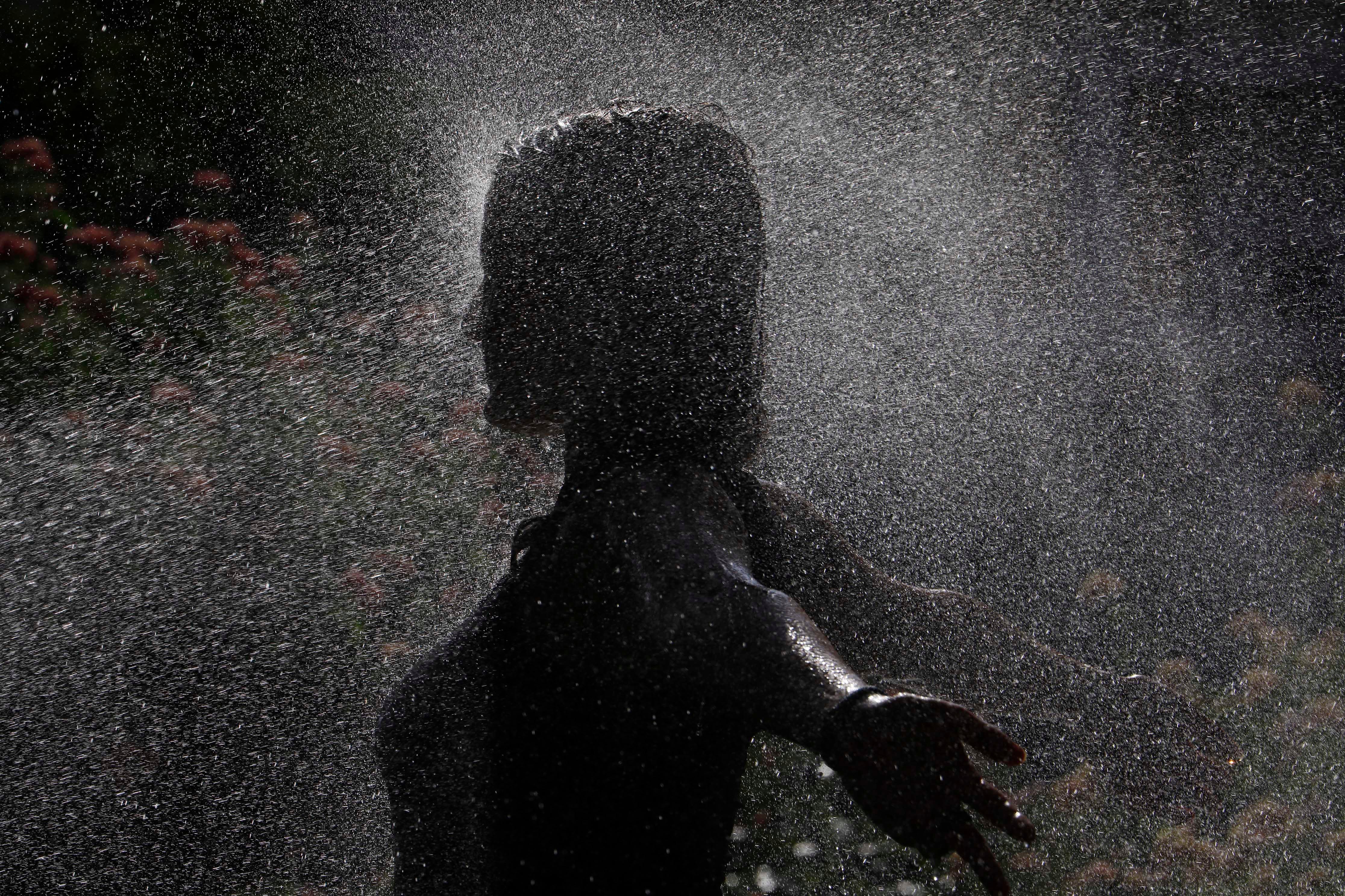 Una joven se refresca gracias a varios aspersores para combatir la ola de calor.