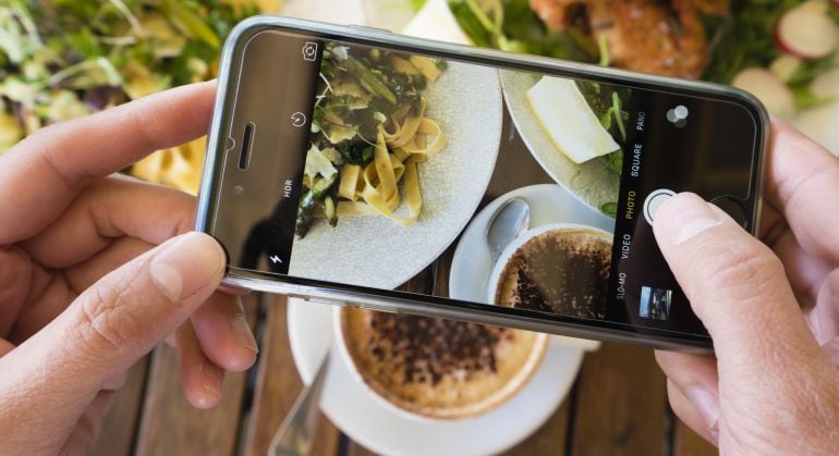 Una mujer sacando una fotografía a su plato de comida. 